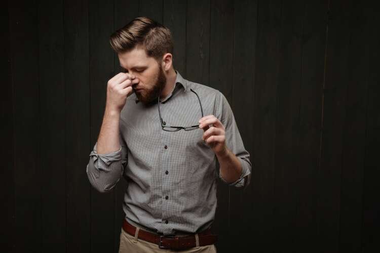Tired bearded man holding glasses, symbolizing entrepreneurial challenges - Global Banking & Finance Review