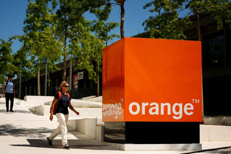 Woman walking past the Orange telecom logo, symbolizing sustainability in finance - Global Banking & Finance Review