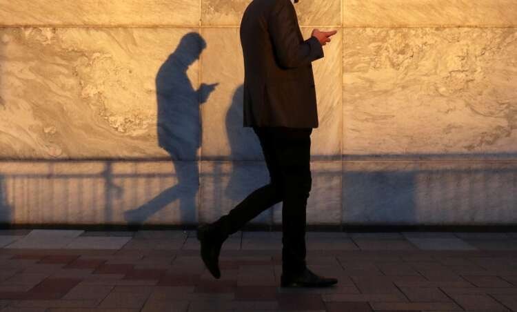 Person using a smartphone in Canary Wharf, reflecting Europe's smartphone market decline - Global Banking & Finance Review