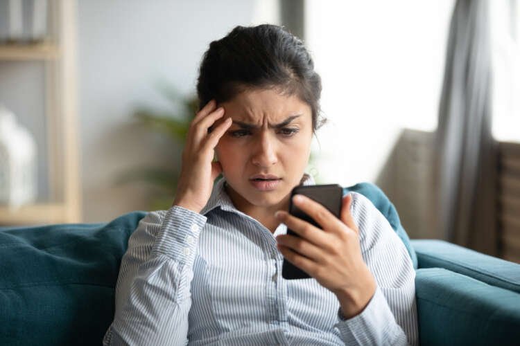 Young woman frustrated with cellphone while dealing with APP fraud issues - Global Banking & Finance Review