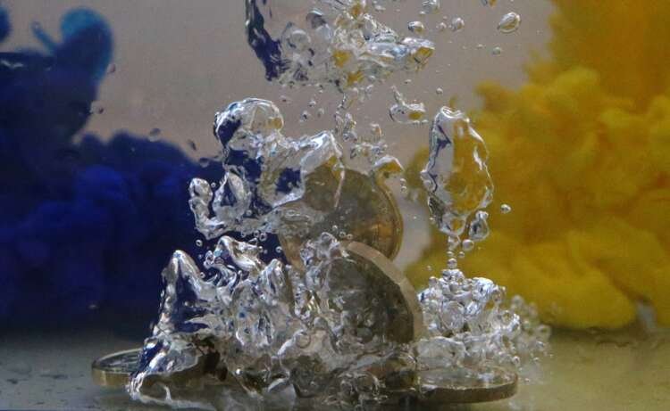 UK pound coins submerged in water with EU flag colors reflecting economic uncertainty - Global Banking & Finance Review