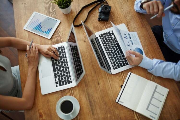 Two employees collaborating with office gadgets while analyzing data in a secure remote work environment - Global Banking & Finance Review