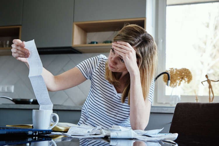 Woman calculating bills in kitchen, representing banks boosting customer loyalty - Global Banking & Finance Review