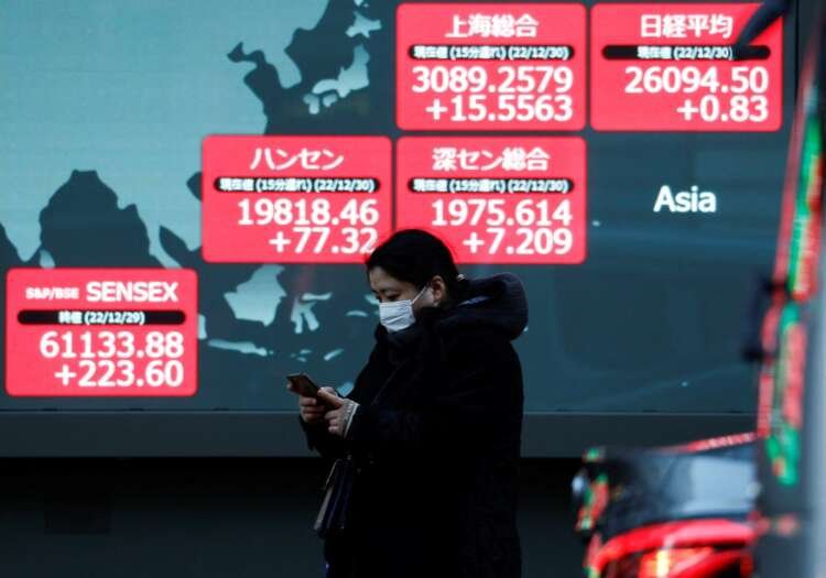 A passerby walks past an electric screen showing Asian stock price indexes amid rate-hike concerns - Global Banking & Finance Review