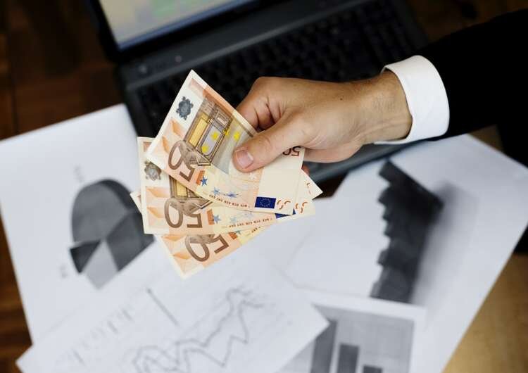 Businessman using a laptop with money in his office, symbolizing Open Banking in Brazil - Global Banking & Finance Review
