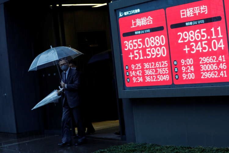 Men holding umbrellas walk near an electric board showing Nikkei index a brokerage in Tokyo