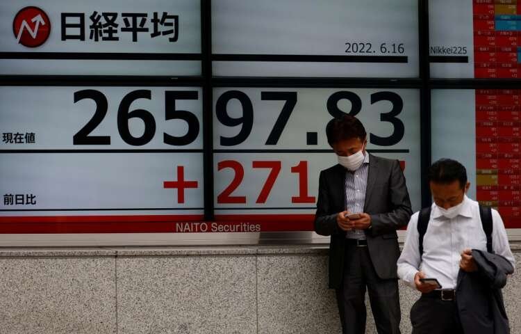 Men in masks using mobile phones in front of Japan's Nikkei index board - Global Banking & Finance Review