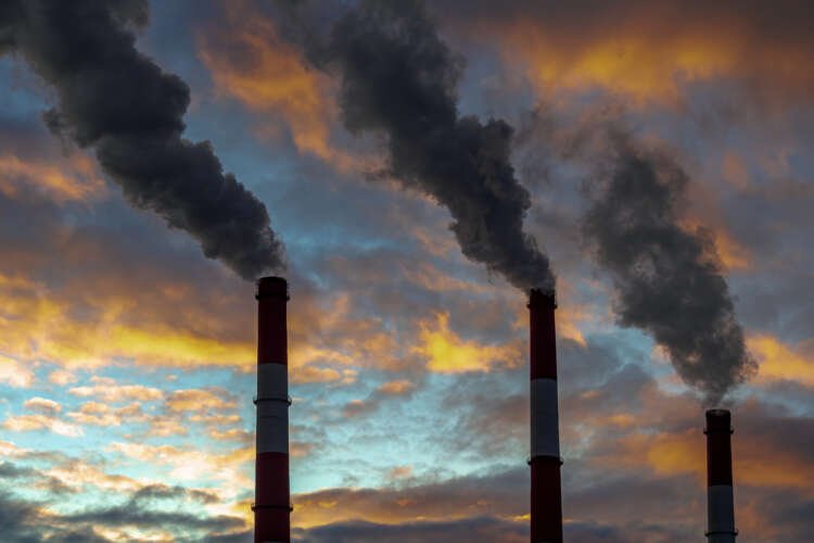 Three smoked pipes releasing emissions against a colorful sky - Climate change and finance risk management - Global Banking & Finance Review