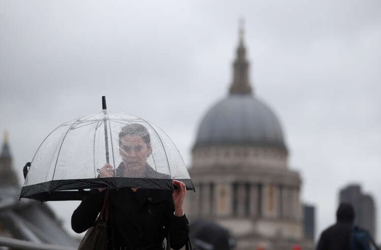 A woman with an umbrella walks across Millennium Bridge, symbolizing women's role in finance - Global Banking & Finance Review