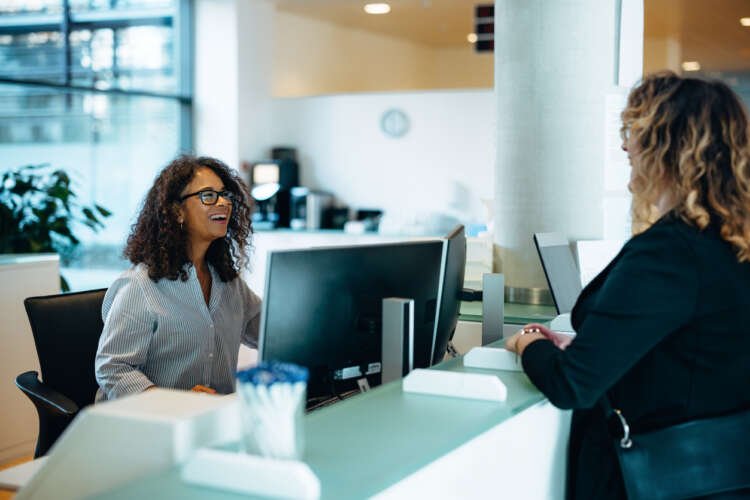 Friendly administrator assisting a woman at the reception desk in an office - Global Banking & Finance Review