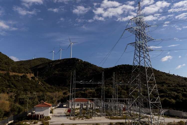 Wind turbines on a hill near a power station, symbolizing Greece's energy subsidies - Global Banking & Finance Review