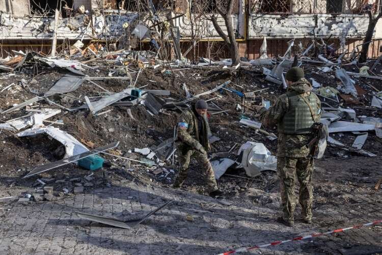 Ukrainian servicemen inspect the area in front of a residential apartment building after it was hit by shelling in Kyiv