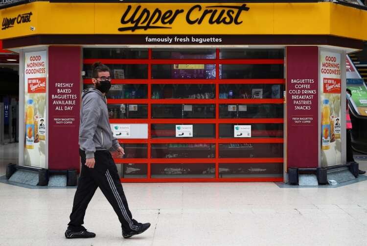 A masked man walks by an Upper Crust outlet at Victoria Station, symbolizing travel recovery amidst inflation concerns - Global Banking & Finance Review