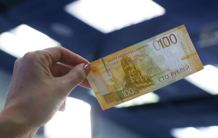A person displays a newly designed Russian 100-rouble banknote amidst currency trading - Global Banking & Finance Review