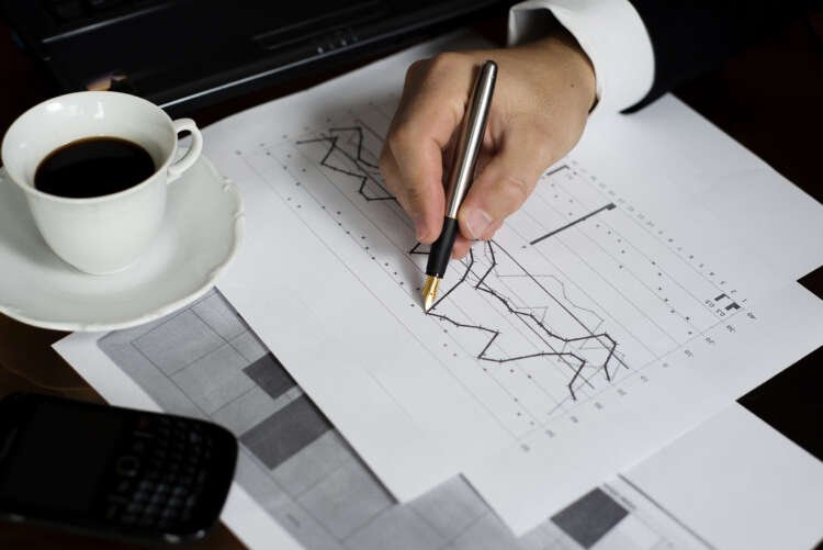 Businessman analyzing interest rates with a laptop and money in an office - Global Banking & Finance Review