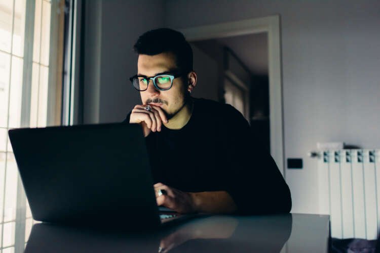 Young man using a computer in an apartment, highlighting financial fraud concerns - Global Banking & Finance Review
