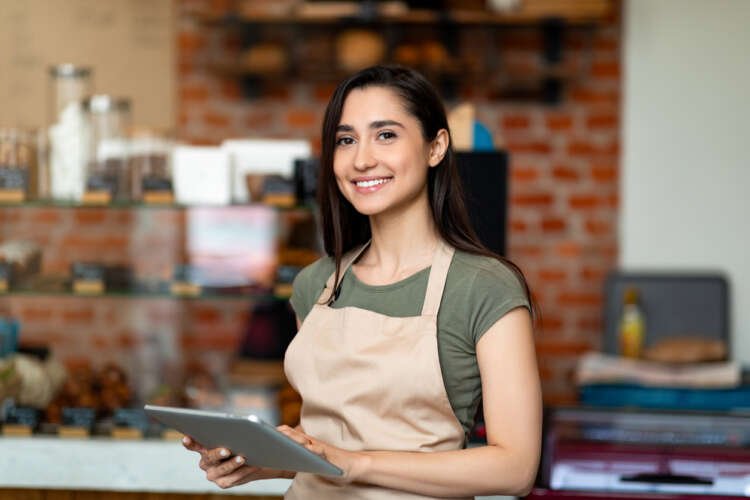 Happy Arab woman in apron holding a digital tablet, representing small business empowerment - Global Banking & Finance Review