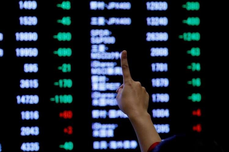 FILE PHOTO: A woman points to an electronic board showing stock prices as she poses in front of the board after the New Year opening ceremony at the Tokyo Stock Exchange (TSE)