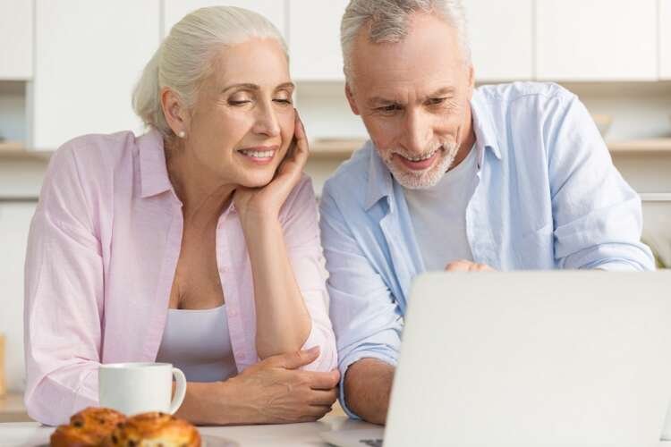 Happy mature couple discussing remortgage options while using a laptop in their kitchen - Global Banking & Finance Review