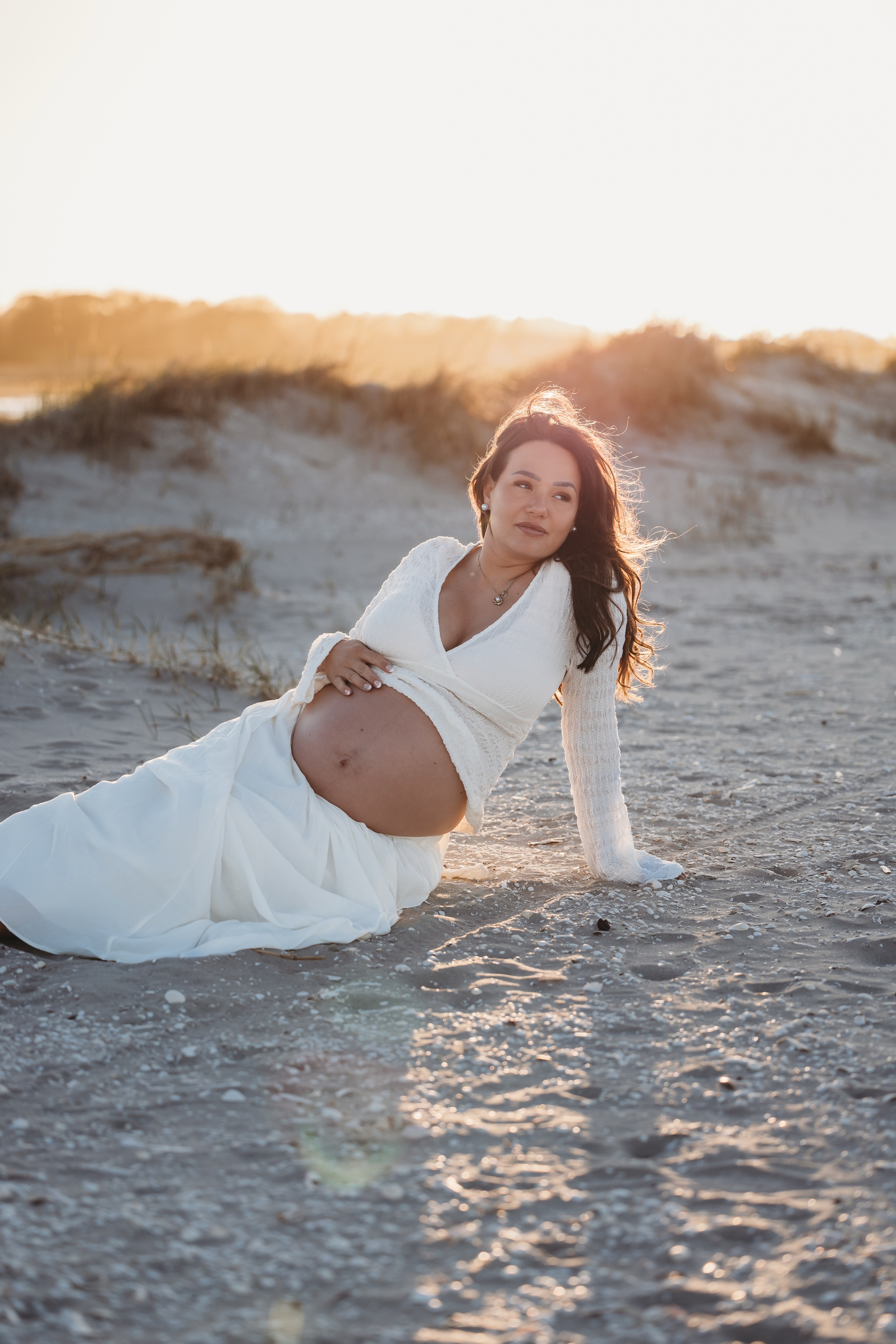 Gravid kvinde siddende i klitterne i solnedgang