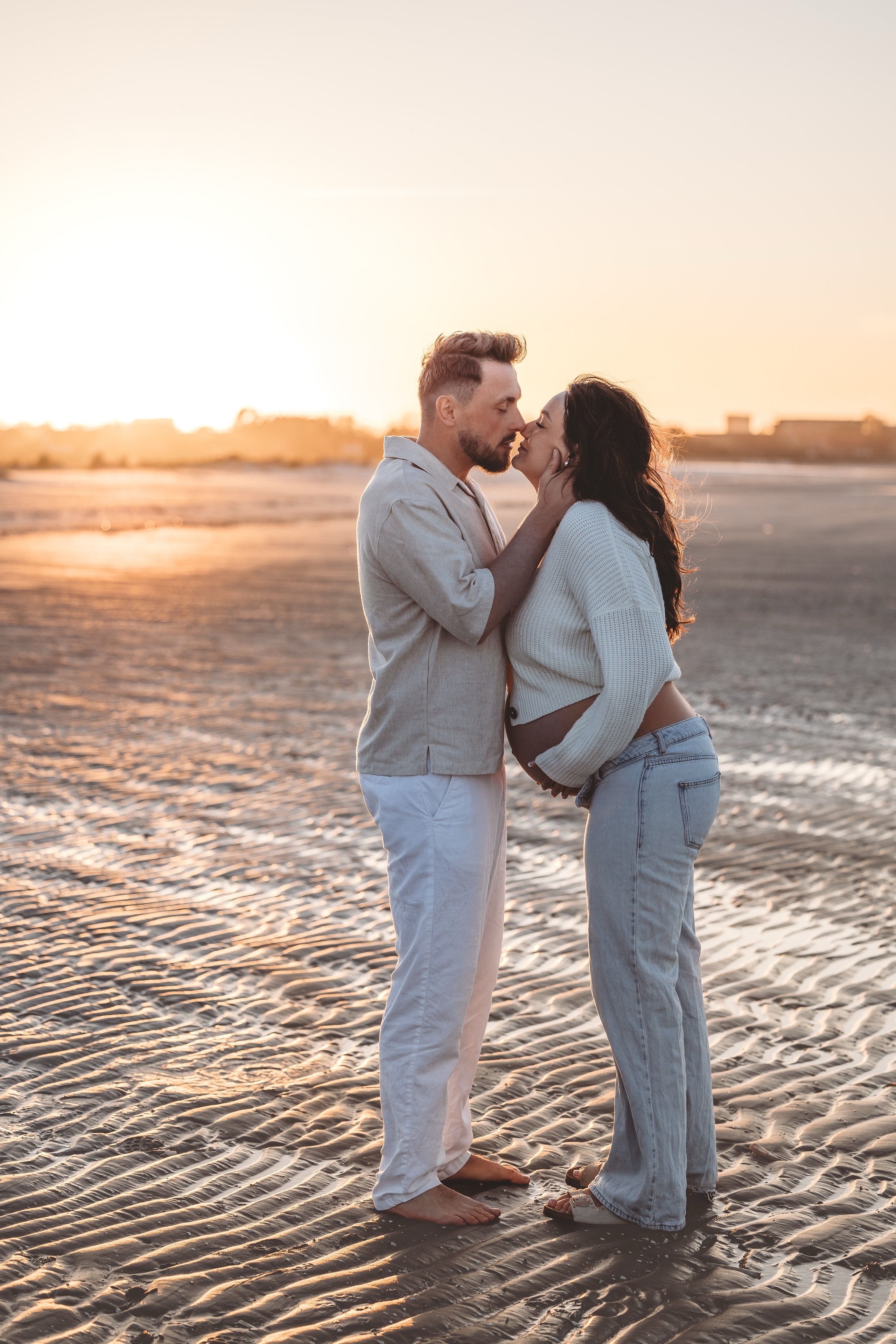Gravidpar i modlys på stranden i solnedgang