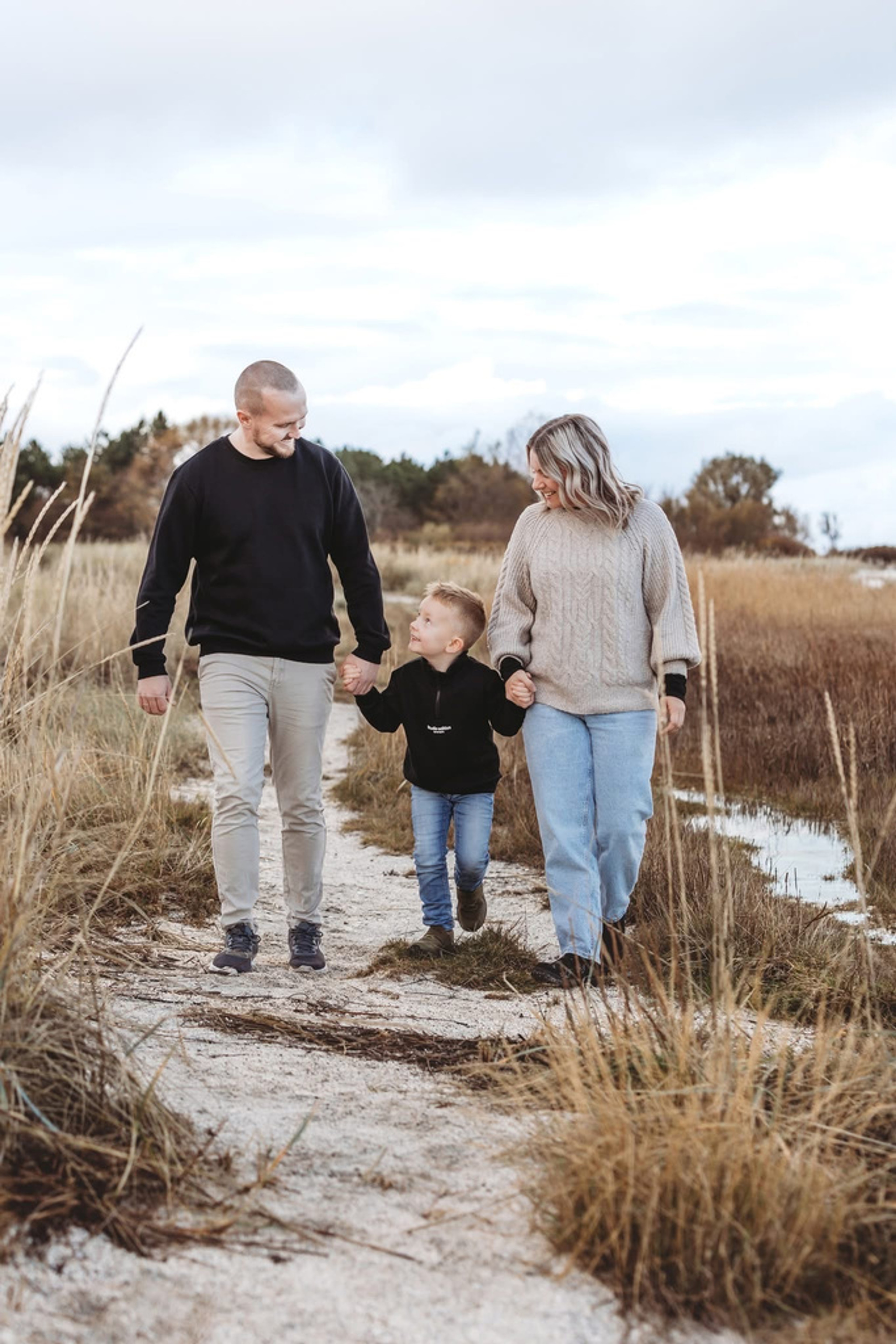 Familie i naturlige farver går i klitlandskab