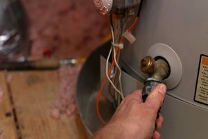 Plumber's hand grabbing drain valve to flush water heater.