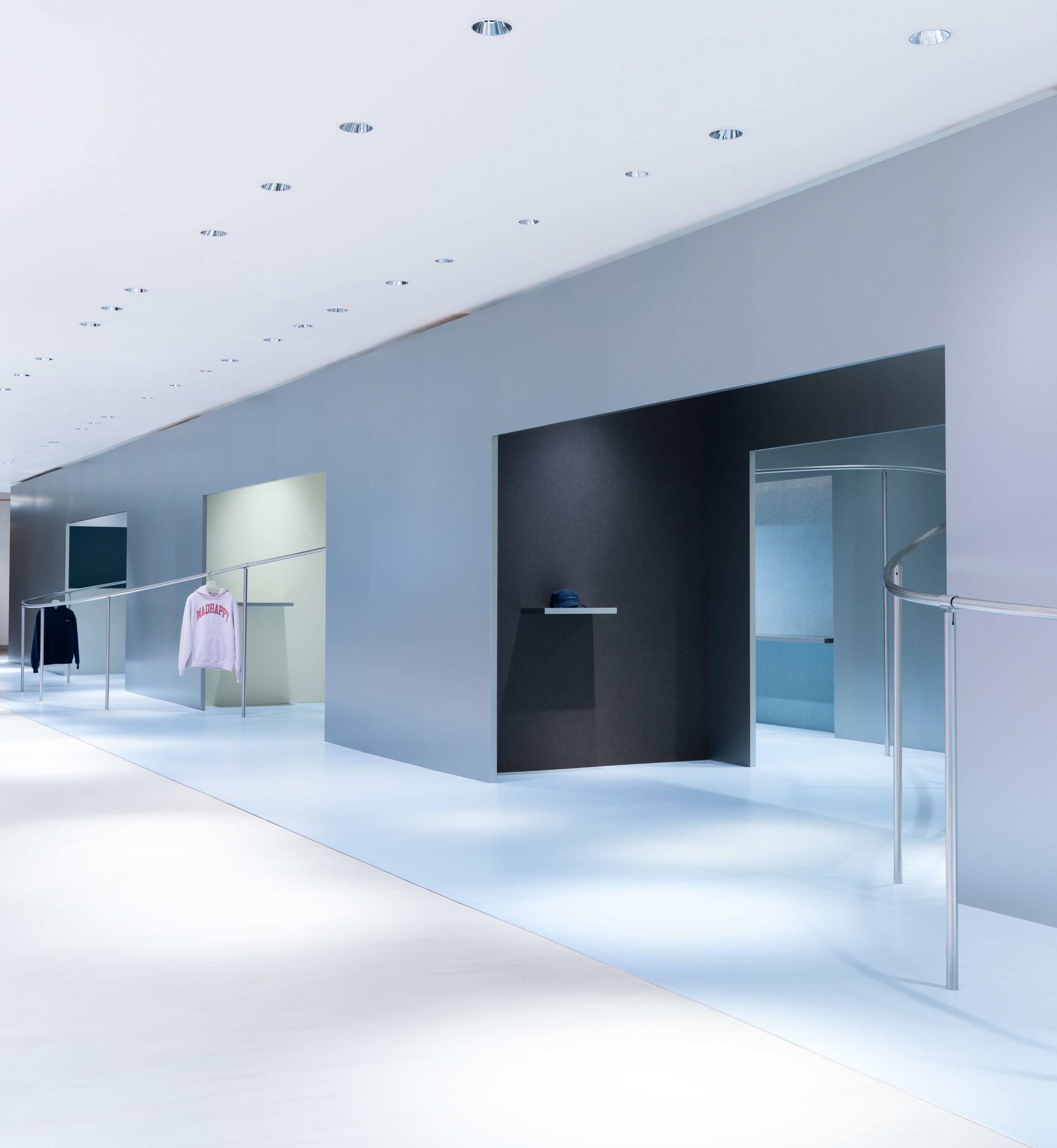A modern, minimalist clothing store interior with white floors, gray walls, recessed lighting, and clothes on display.
