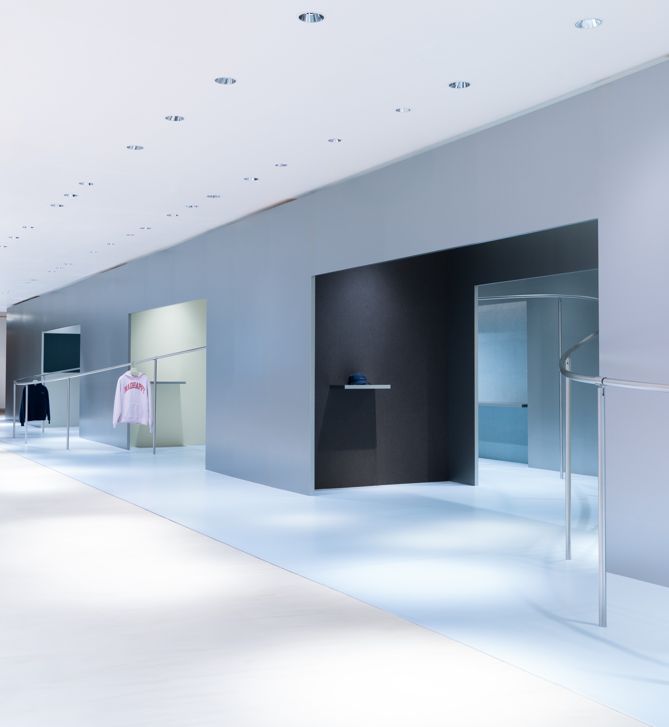 A modern, minimalist clothing store interior with white floors, gray walls, recessed lighting, and clothes on display.