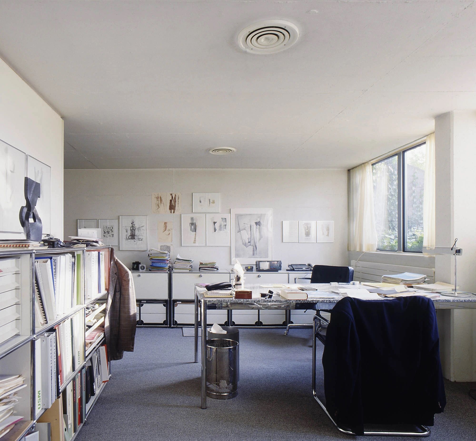 a room with a desk , chairs , shelves and windows .