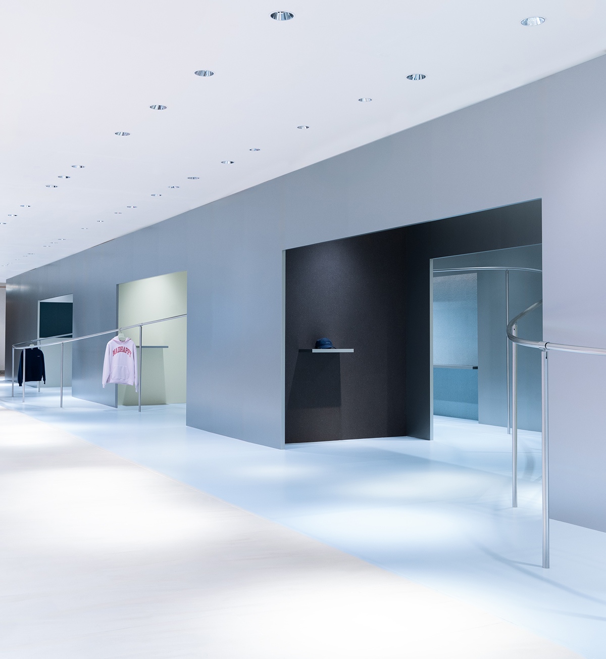 A modern, minimalist clothing store interior with white floors, gray walls, recessed lighting, and clothes on display.