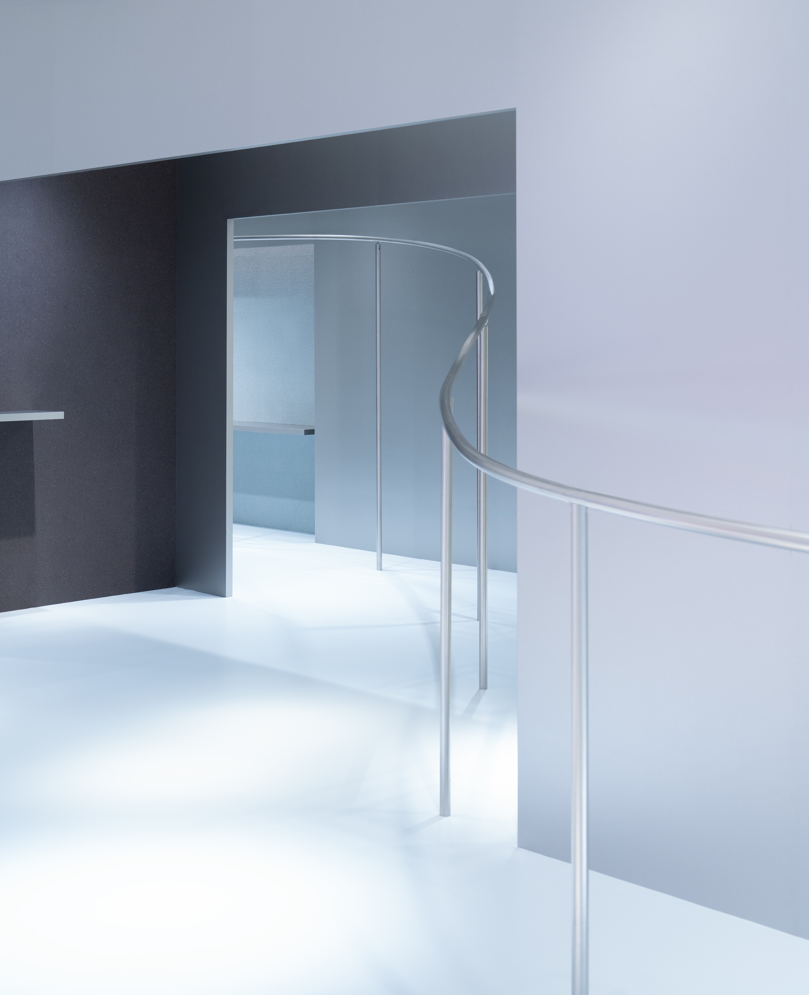 Minimalist interior with a curved silver railing and light blue-grey tones.