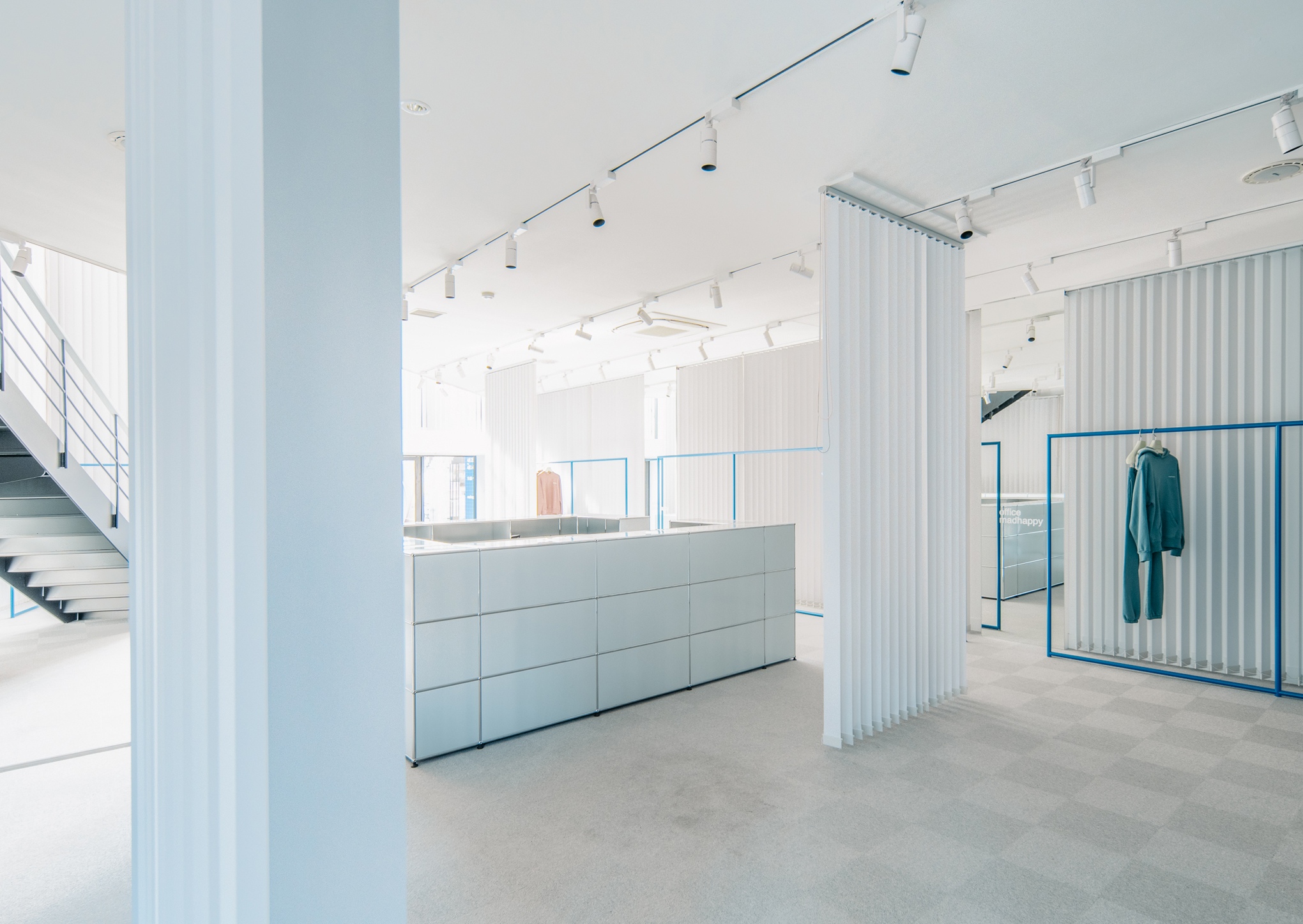 a large white room with a staircase and clothes hanging on racks .