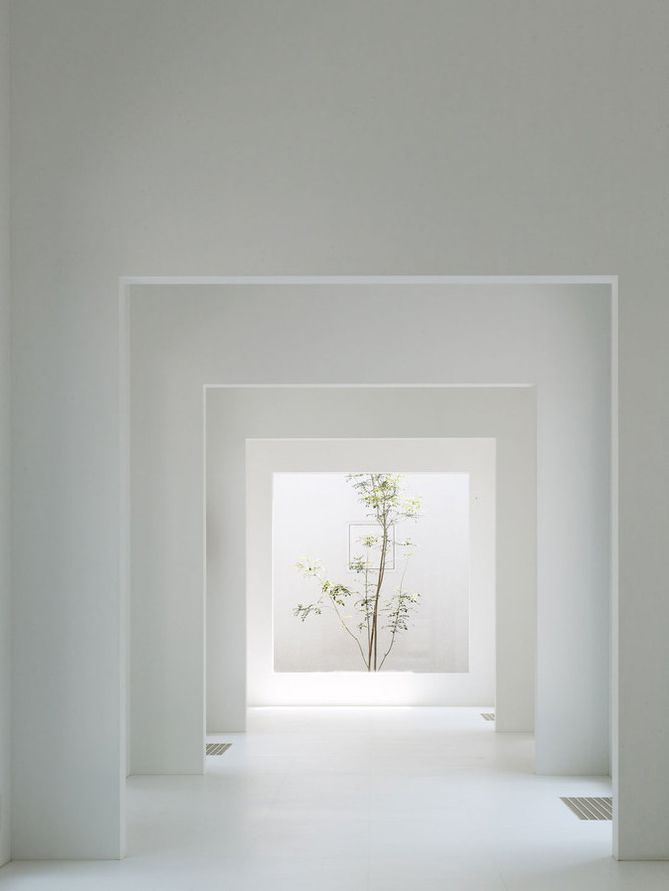 Minimalist white interior with receding rectangular frames leading to a bright opening with a green tree.
