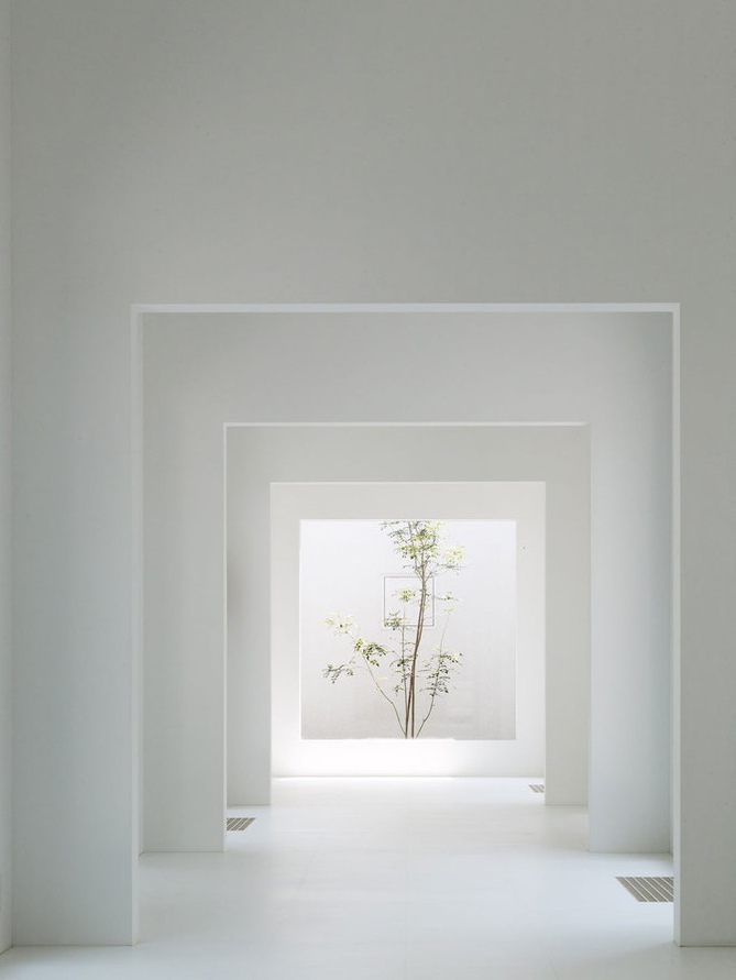 Minimalist white interior with receding rectangular frames leading to a bright opening with a green tree.