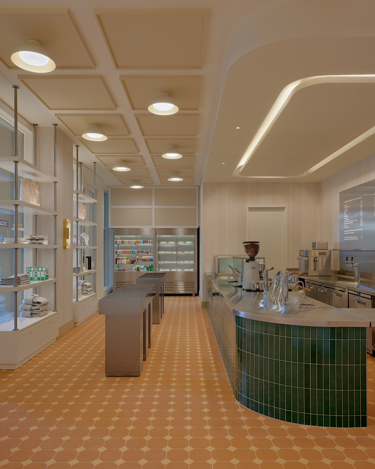 Modern cafe interior with an orange patterned floor, a green-tiled service counter, and white display shelves.