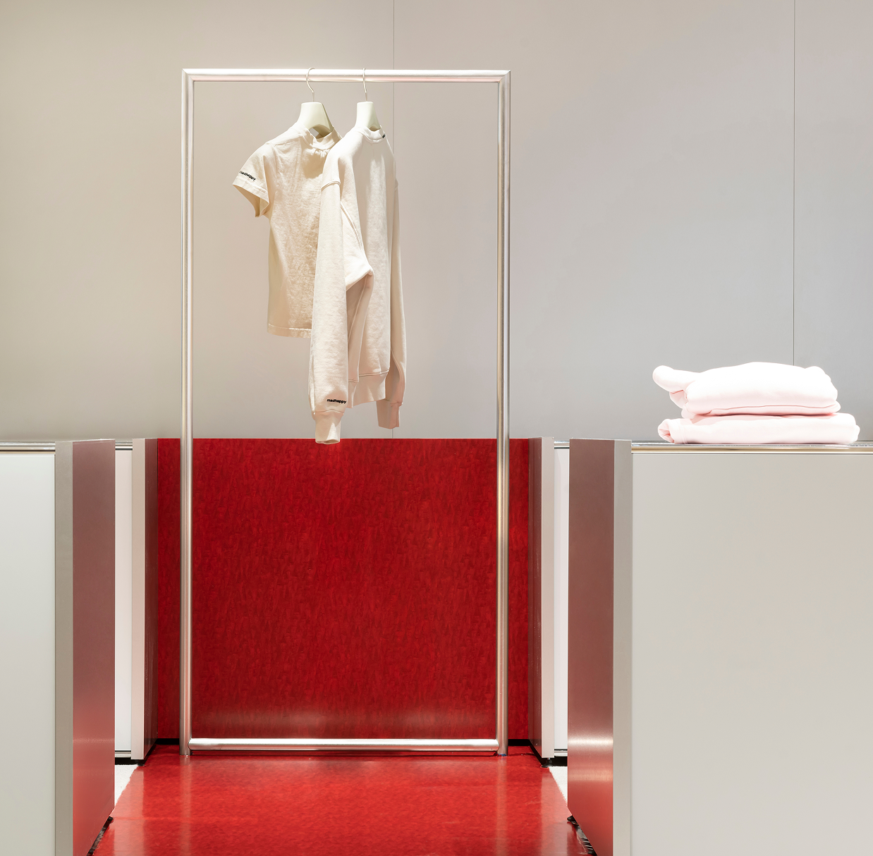 Cream t-shirt and sweatshirt on a silver rack, with folded pink garments on a shelf, in a red and gray interior.