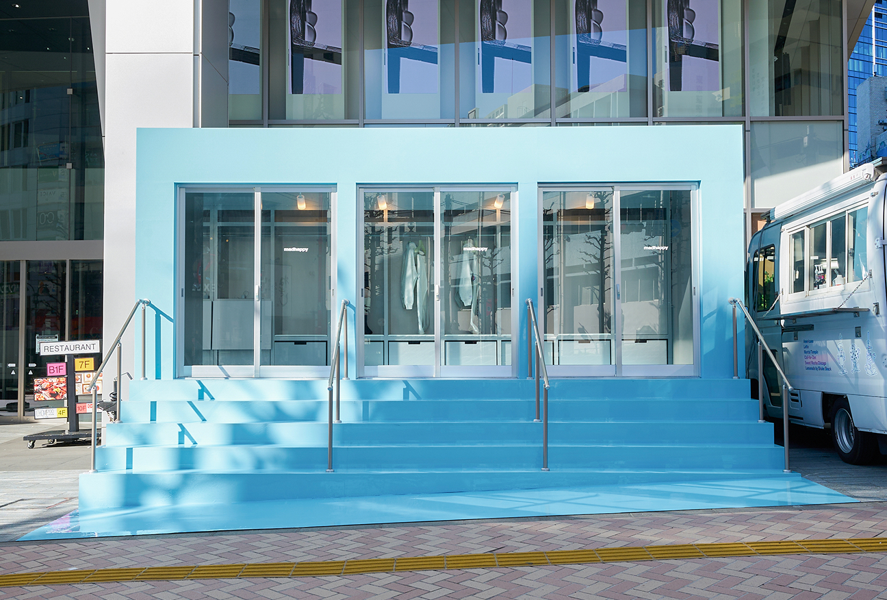 A light blue storefront with three glass display windows, accessed by wide matching steps with handrails.
