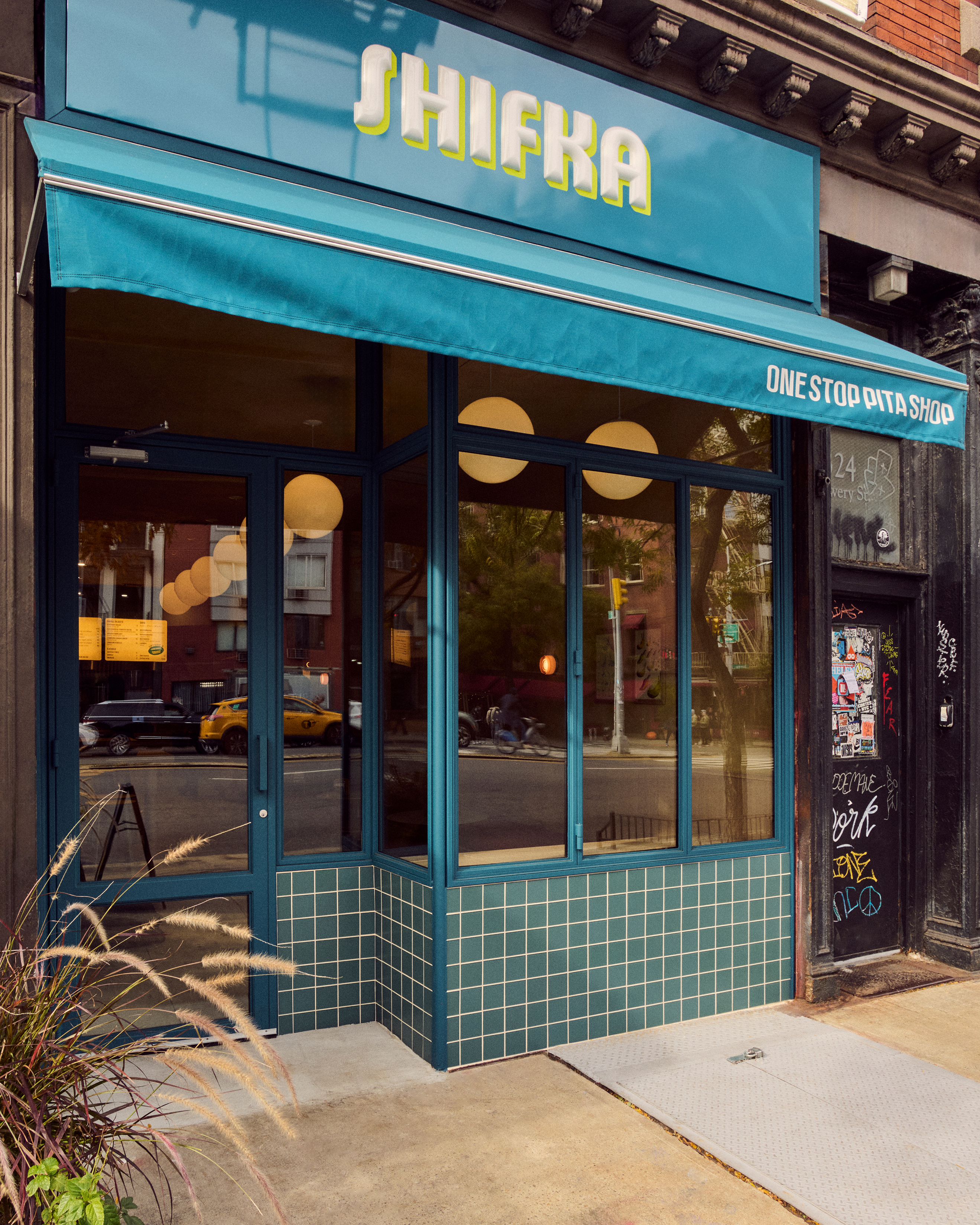 Shifka One Stop Pita Shop storefront with a turquoise awning, teal window frames, and matching tiled facade.