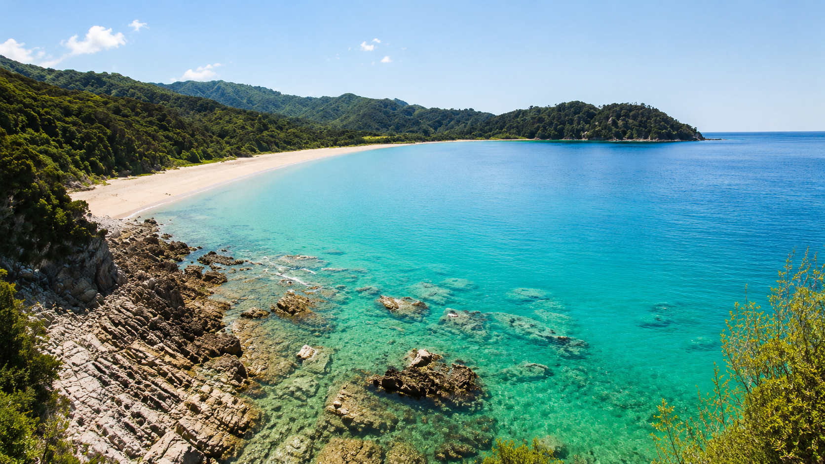 Sweeping turquoise bay with a white sand beach and a rocky shore below bush-covered hills
