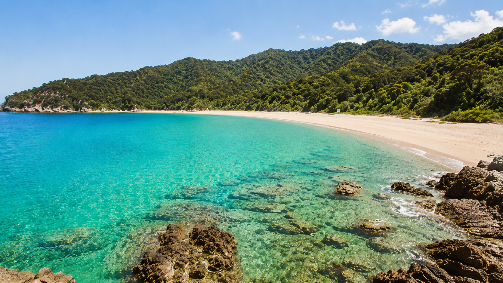 Golden sand beach curving around a clear turquoise bay below forested hills