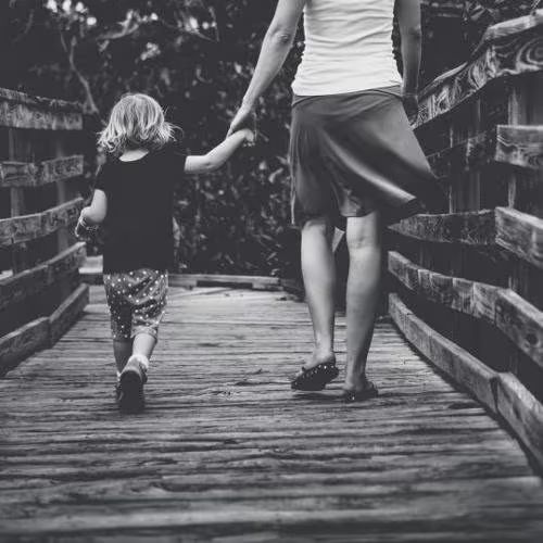 Young child holding a parent's hand on a wooden bridge