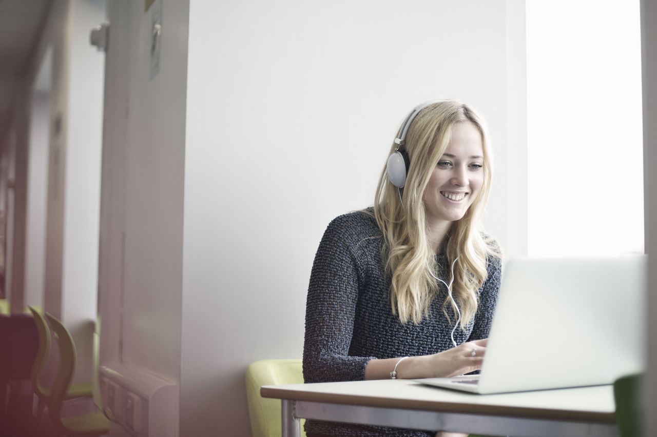 Woman wearing headphones and smiling while typing on a laptop.