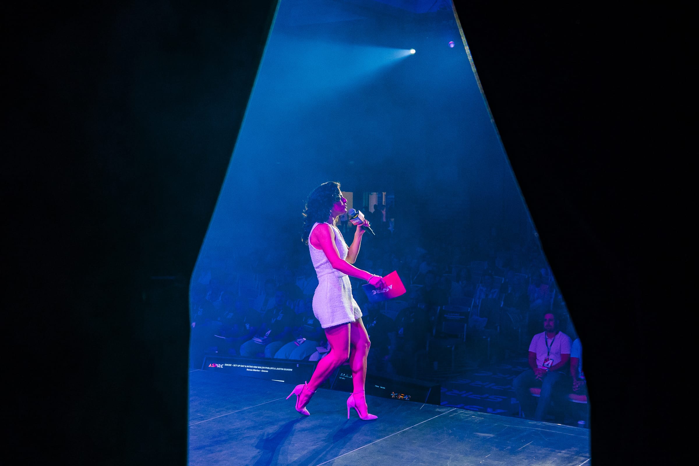 Renée speaking onstage under a spotlight at the Aspire Tour