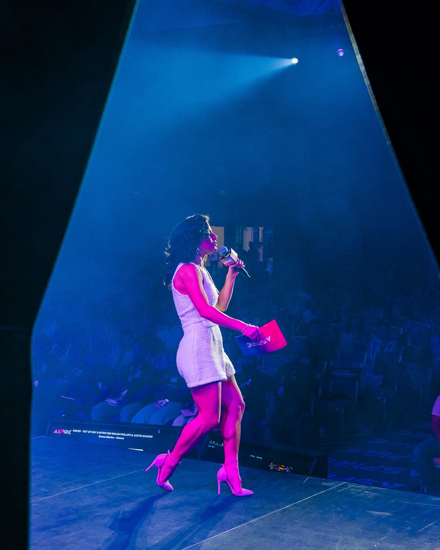 Renée speaking onstage under a spotlight at the Aspire Tour