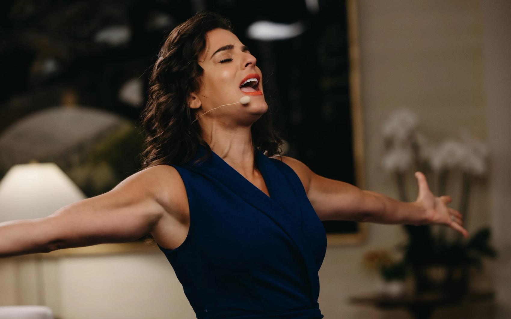 Renée Marino speaking with her arms open to an audience