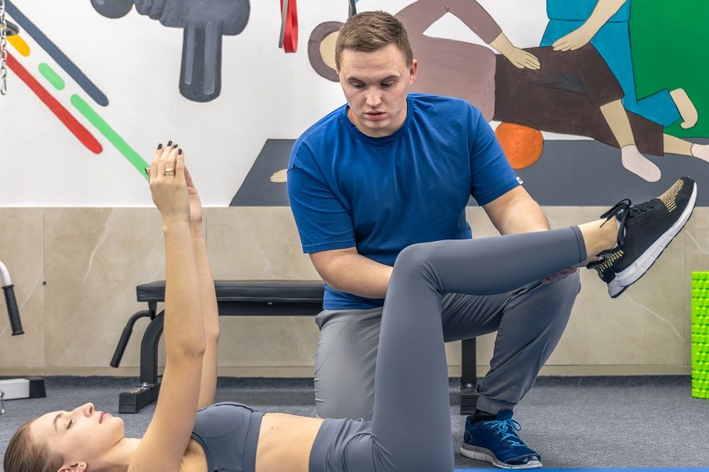 Kineziterapeutas koreguoja ant nugaros gulinčios sportuojančios moters kojos judesį