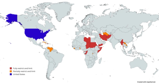 Graphic world map highlighting nations under President Trump’s 2025 travel ban—red for fully restricted countries (Afghanistan, Burma/Myanmar, Chad, Republic of the Congo, Equatorial Guinea, Eritrea, Haiti, Iran, Libya, Somalia, Sudan, Yemen), orange for partially restricted countries (Burundi, Cuba, Laos, Sierra Leone, Togo, Turkmenistan, Venezuela), with the United States marked in blue.