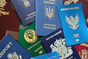 A collection of international passports from various countries, including the United Kingdom, Ukraine, Indonesia, Nigeria, Brazil, and Portugal, arranged in an overlapping layout. Each passport features its unique color, emblem, and text in different languages.