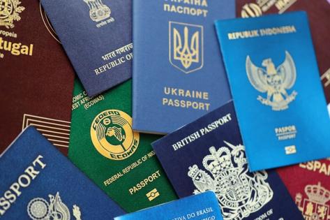 A collection of international passports from various countries, including the United Kingdom, Ukraine, Indonesia, Nigeria, Brazil, and Portugal, arranged in an overlapping layout. Each passport features its unique color, emblem, and text in different languages.